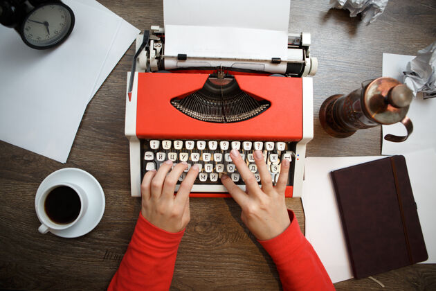 打字机女人手上的老式红色打字机与空白纸的木桌上开始俯视图字母