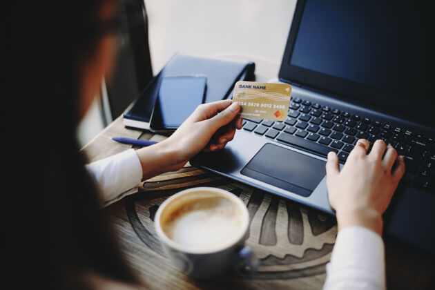 个人在咖啡店喝咖啡时 一只手拿着塑料信用卡和笔记本电脑进行网上交易商店在线购物