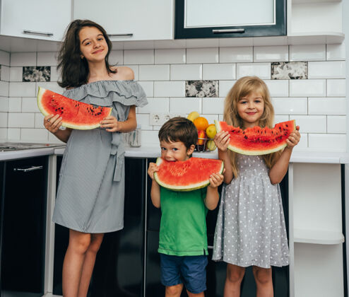 健康三个快乐微笑的孩子在厨房里吃西瓜健康咬童年