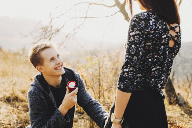 快乐帅气的年轻人带着戒指盒微笑着向匿名女士求婚 同时在大自然中共度时光惊喜无脸阳光
