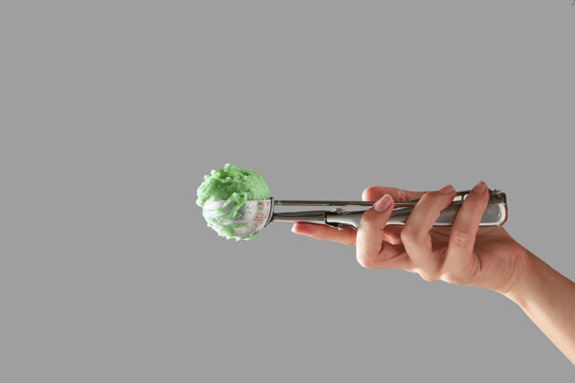 自制一只雌性的手拿着一个金属勺子 里面放着绿色水果冰淇淋 放在灰色的墙上 墙上留有足够的空间文本冷夏日甜点冰设备持有