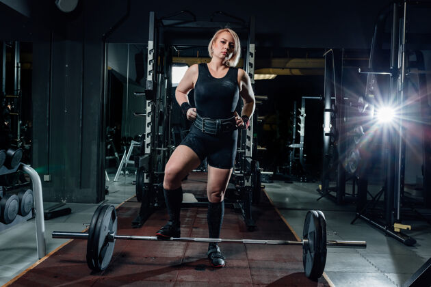健身房穿着运动服的自信女人站在黑暗的现代体育馆里看着镜头女子健康肌肉