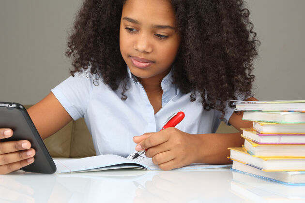孩子皮肤黝黑的女孩拿着智能手机做作业学习女孩笔记本