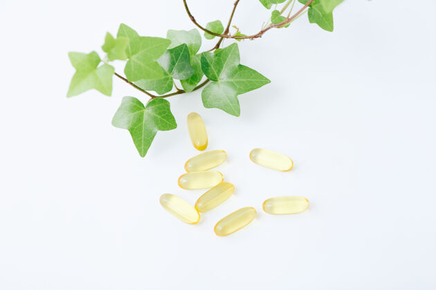 草药鱼油维生素胶囊和绿叶上的白色治疗植物医学