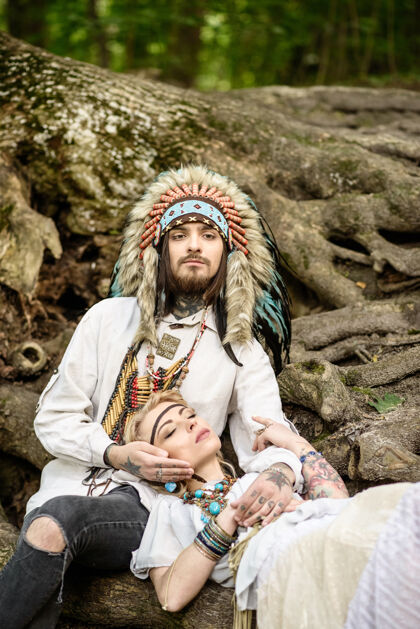 快乐一对年轻的美国印第安夫妇躺在一棵大树的树根上关怀印第安人浪漫