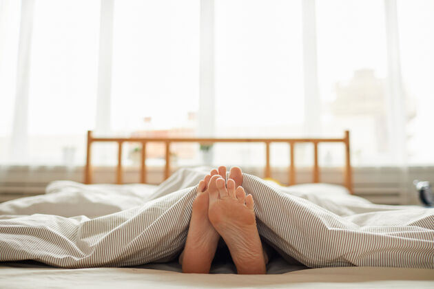 早晨一个赤脚躺在床上毯子下的年轻女子的特写镜头毯子放松床