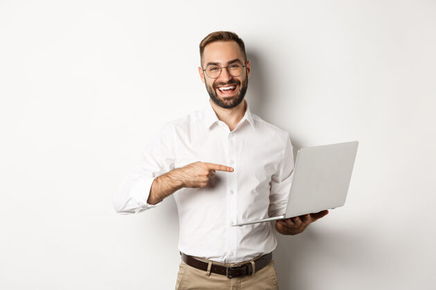 Male公事公办 帅哥经理戴着眼镜在笔记本电脑上工作 指着电脑高兴地笑着 站在白色的背景上BusinessManPointingAgent