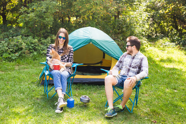 帐篷人们 夏季旅游和自然概念-年轻夫妇坐在帐篷附近纽带火微笑