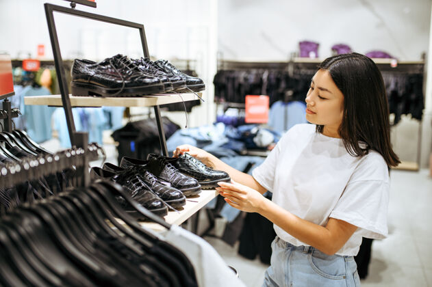 人穿衣服选鞋的年轻女子女店员在时尚精品店购物的人 购物狂 穿靴子的购物者穿着衣服消费主义