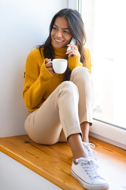 女孩一个快乐的女人坐在窗边 隔着灰墙 喝着咖啡 打电话移动惊喜内容