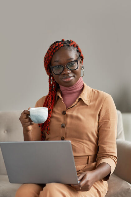 互联网一个年轻的非洲裔美国妇女拿着咖啡杯和笔记本电脑在家里享受工作的垂直肖像成功企业家使用