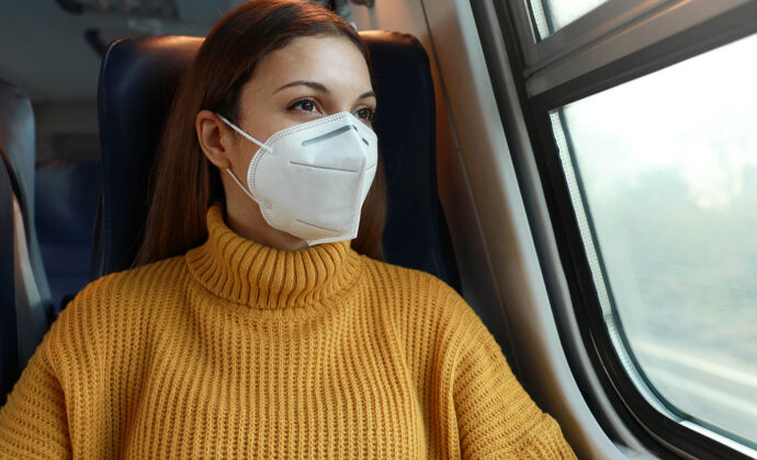 面具戴着口罩的年轻女商人从火车窗口望出去保护坐着年轻人