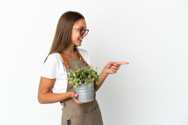 手势园丁女孩拿着植物在孤立的白色背景指指点点的一边 并提出了一个产品表情指点微笑