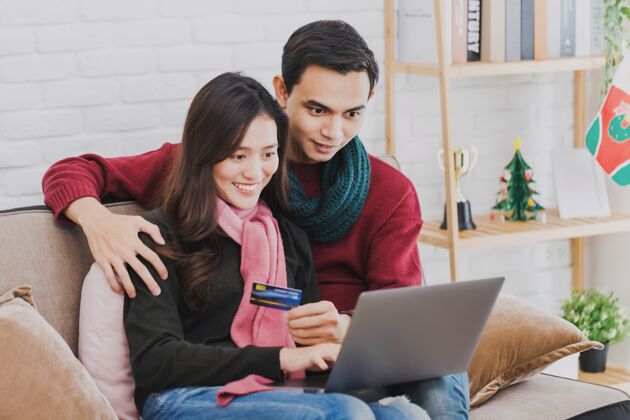 女人年轻的亚洲情侣用信用卡和笔记本电脑在线购物肖像一起微笑