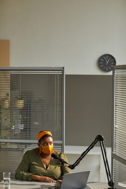 商务人士戴着防护面具的年轻电台dj坐在桌旁 拿着笔记本电脑 对着麦克风讲话笔记本电脑主持成人