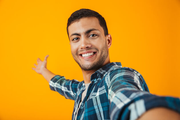 站着一个穿着格子衬衫的年轻人孤零零地站在橙色的墙上 自拍抱着自拍拍摄