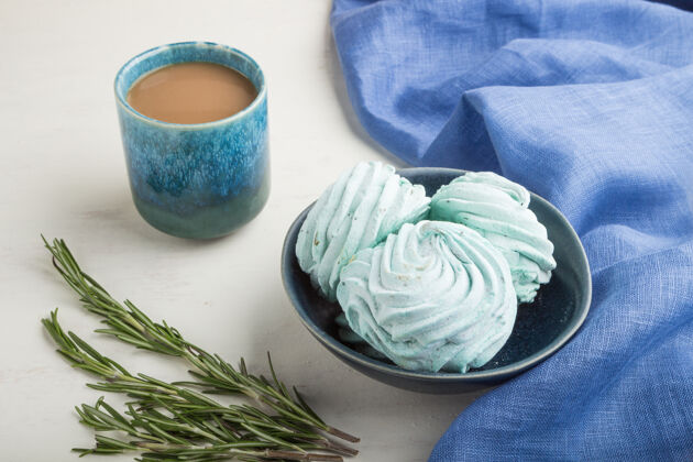 糖蓝色的自制西风或棉花糖 在白色木制表面上放一杯咖啡和蓝色纺织品浪漫小吃甜点