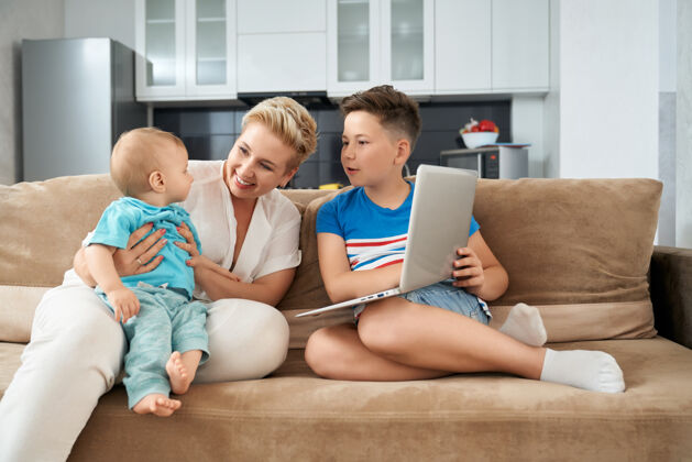 家庭微笑的妈妈带着两个儿子在沙发上玩电脑使用一起