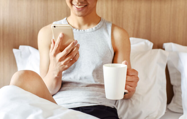 失眠一个十几岁的男孩在卧室里用他的智能手机和拿着一杯咖啡床困难觉醒