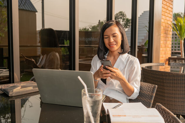 使用一个女商人在咖啡馆用笔记本电脑和手机的画像坐着女孩自由职业者