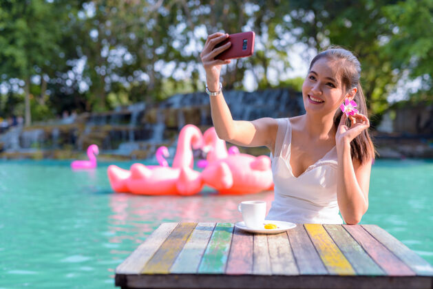 马尾辫年轻美丽的亚洲女游客在湖边户外放松的画像手机微笑虚拟博客