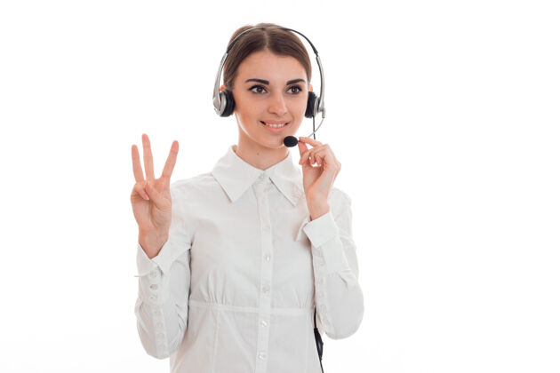 工作年轻迷人的呼叫中心接线员穿着白衬衫 耳机孤立在录音室的墙上销售接线员年轻
