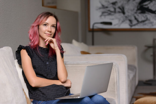 沙发美丽的商人肖像与粉红色的头发使用笔记本电脑在客厅从家办公的概念休闲数码笔记本电脑