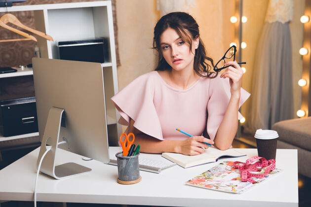 人穿着粉色豪华连衣裙的年轻时尚女士在办公室用电脑工作衣服包收藏