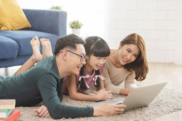 玩耍快乐的亚洲家庭一起在家客厅的沙发上使用笔记本电脑可爱学习使用