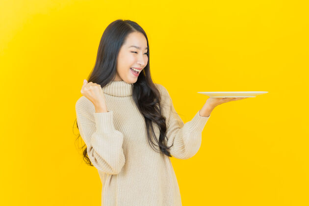 快乐画像美丽的亚洲年轻女子微笑着黄色墙上的空盘子杯子亚洲肖像