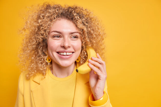 請樂觀的卷發女子笑容可掬地把香蕉抱在耳邊 仿佛在打電話似的 帶著夢幻般的表情遠遠望去 隔著黃色的墻紙空間高興人牙齒