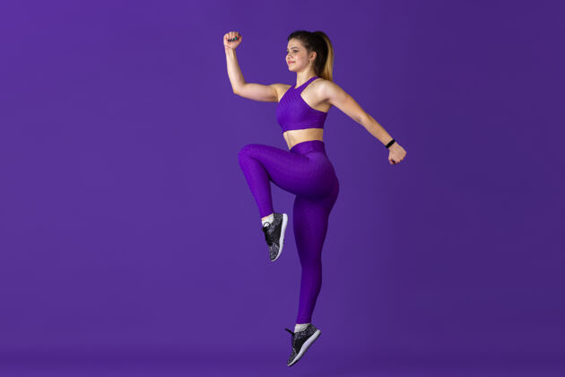紧缩在跳跃年轻漂亮的女运动员在练习 单色紫色肖像运动型白种人适合模型训练健美 健康的生活方式 美丽和行动的概念人举重运动