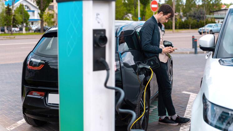 汽车男人在充电站给他的电动车充电 用智能手机环境汽车电池