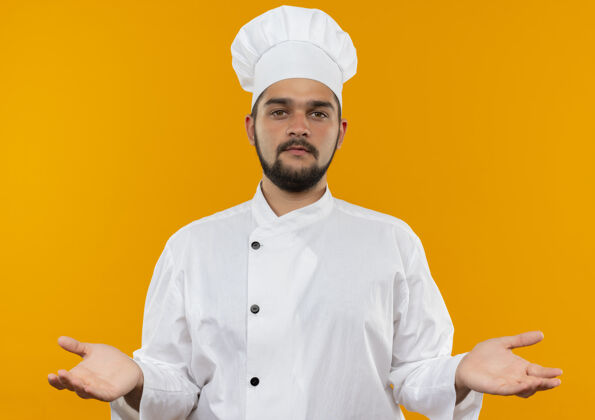 厨师自信的年轻男性厨师身着厨师制服 双手空空地孤零零地站在橙色的墙上年轻空虚男性