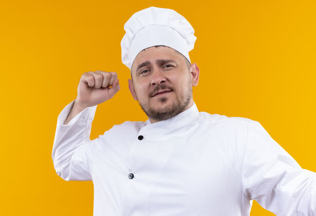厨艺自信的年轻帅哥厨师身着厨师制服 举起拳头孤立在橙色的墙上年轻自信拳头