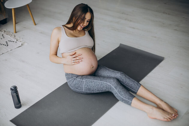 为人父母孕妇在家里的垫子上练习瑜伽普拉提分娩女性