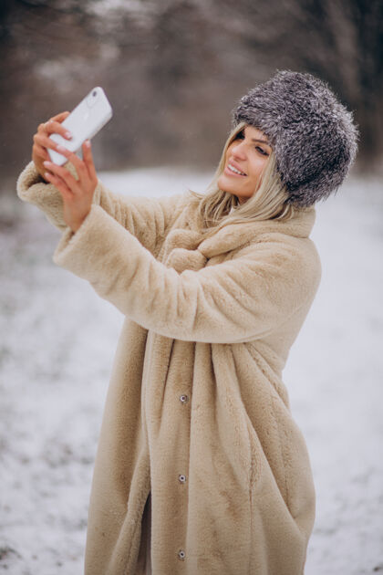 户外穿着冬衣的女人走在满是雪的公园里打电话电话探索自然