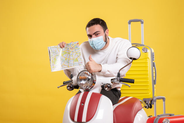 面具旅行概念的俯视图 戴着医用面罩的年轻人站在摩托车旁边 黄色手提箱在上面 拿着地图做着ok手势地图手势人
