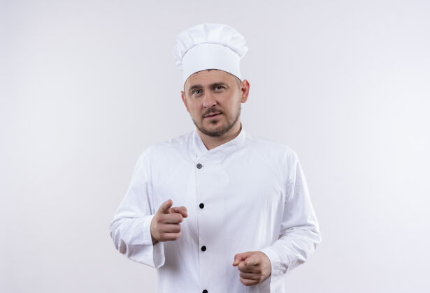 厨艺自信的年轻帅哥厨师穿着厨师制服指着隔离在白墙上指点自信帅气