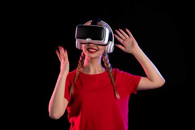 人物戴着耳机在黑暗的墙上玩虚拟现实的年轻女士的正视图年轻女士女士成人