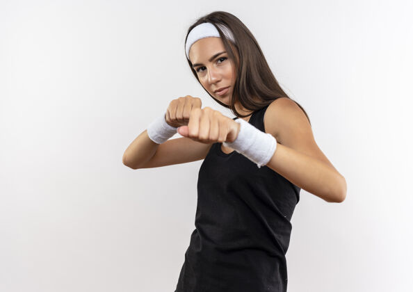 运动自信漂亮的运动女孩戴着头带和腕带做拳击姿势隔离在白色墙壁与复制空间头带拳击穿