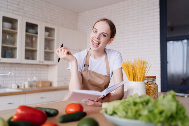 切割厨房里穿着围裙的年轻美女在新鲜蔬菜旁写下她最喜欢的食谱学习围裙厨房