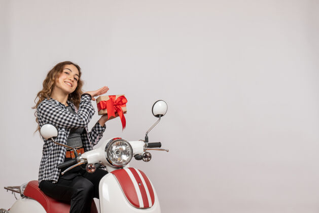 时尚骑着轻便摩托车的漂亮女孩手里拿着灰色的礼物汽车摩托车礼品