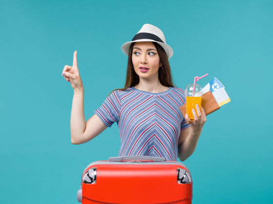 旅行前视图：度假中的女人拿着她的红包 拿着蓝色背景上的票和果汁 旅途中的度假女人微笑包女