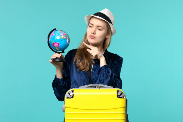 准备正面图年轻女子手持地球仪 准备在淡蓝色背景上度假女性旅程航海飞机度假举行微笑成人