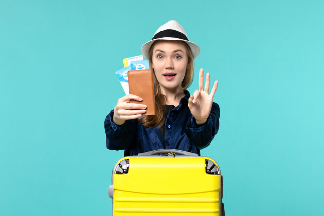 机票前视图年轻女子拿着机票 准备在淡蓝色背景下旅行海上度假旅行飞机旅行工作旅行微笑
