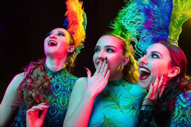 女性美丽的年轻女子在狂欢节 时尚的化装服装与羽毛在霓虹灯下的黑色墙壁德人女人