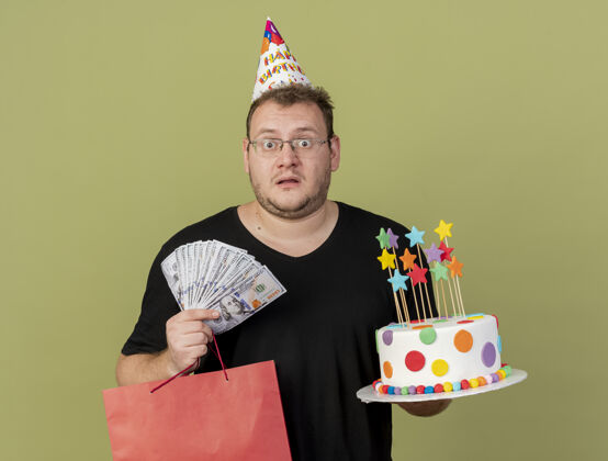 帽子震惊的成年斯拉夫人戴着眼镜 戴着生日帽 手里拿着钱 纸 购物袋和生日蛋糕纸成人包