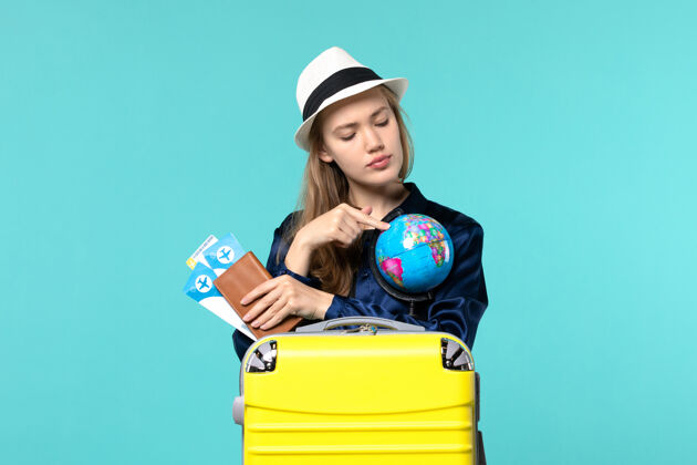钱包正面图年轻女子拿着钱包拿着蓝色地板上的机票飞行女子旅行海上度假人航行微笑