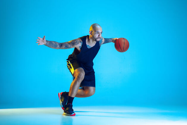球年轻的篮球队员穿着运动服训练 在行动中练习 在霓虹灯下隔离在蓝色的墙上球员专业人